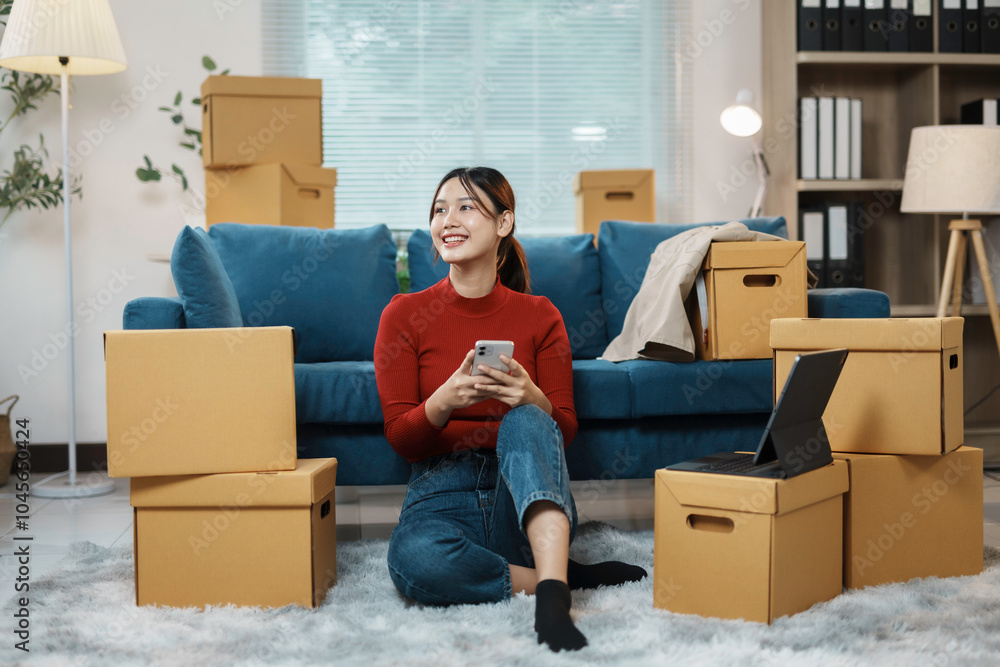 Smiling young woman relaxing on floor using smartphone surrounded by cardboard boxes, happy homeowner moving into new house Smiling young woman relaxing on floor using smartphone surrounded by cardboard boxes, happy homeowner moving into new house