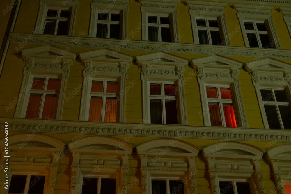 Fototapeta premium A tall building that features numerous windows is brightly lit up during the night, showcasing its beautiful facade and architecture