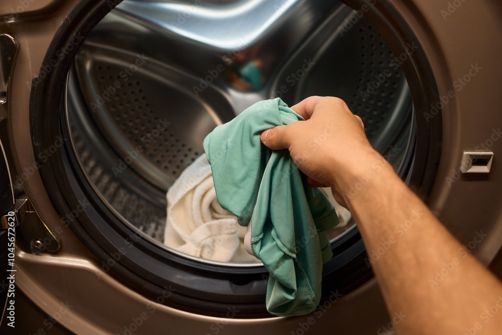 A person is loading various clothes into a washing machine to get them clean and fresh A person is loading various clothes into a washing machine to get them clean and fresh