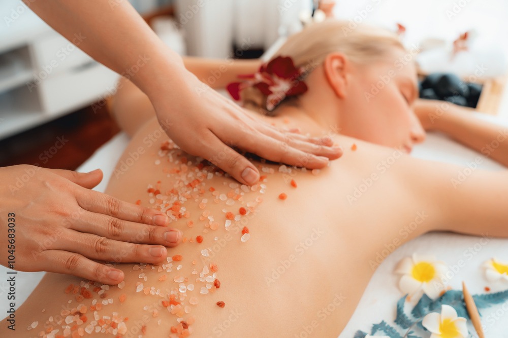 Closeup woman customer having exfoliation treatment in luxury spa salon with warmth candle light ambient. Salt scrub beauty treatment in health spa body scrub. Quiescent Closeup woman customer having exfoliation treatment in luxury spa salon with warmth candle light ambient. Salt scrub beauty treatment in health spa body scrub. Quiescent