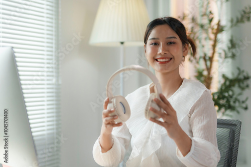 Young asian businesswoman holding headphones smiling while working from her home office