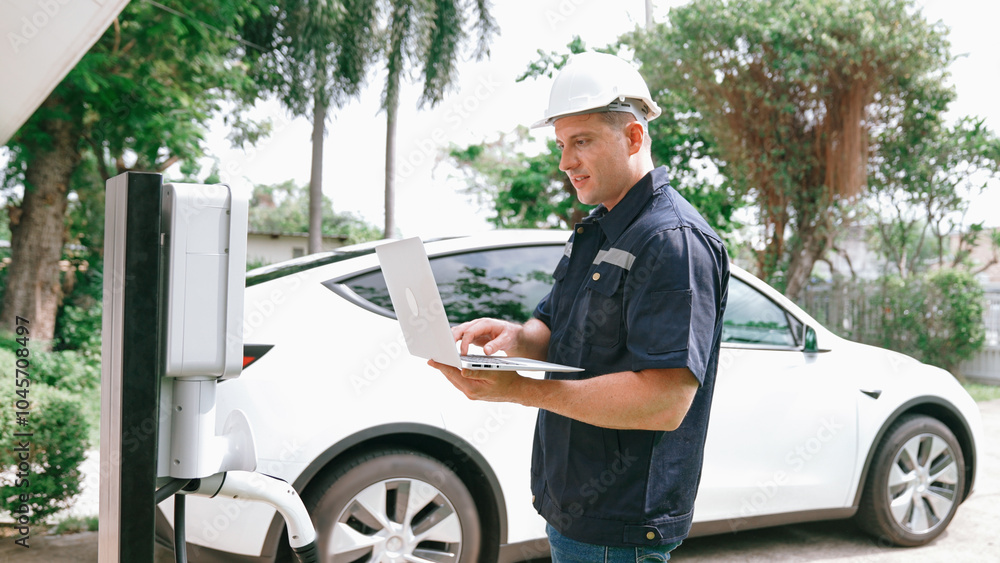 Qualified technician working on home EV charging station installation, making troubleshooting and configuration setup on charging system with laptop for EV at home. Synchronos Qualified technician working on home EV charging station installation, making troubleshooting and configuration setup on charging system with laptop for EV at home. Synchronos