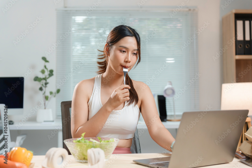 Young asian woman is enjoying a healthy salad while working on her laptop in her home office Young asian woman is enjoying a healthy salad while working on her laptop in her home office