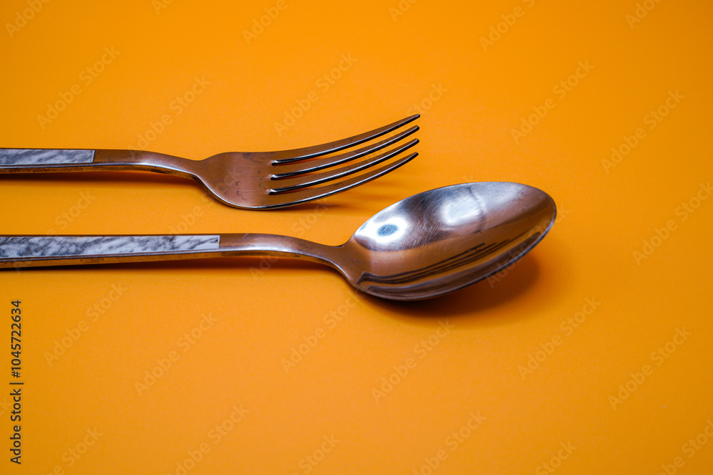 A pair of spoons and forks on an orange background. A pair of spoons and forks on an orange background.