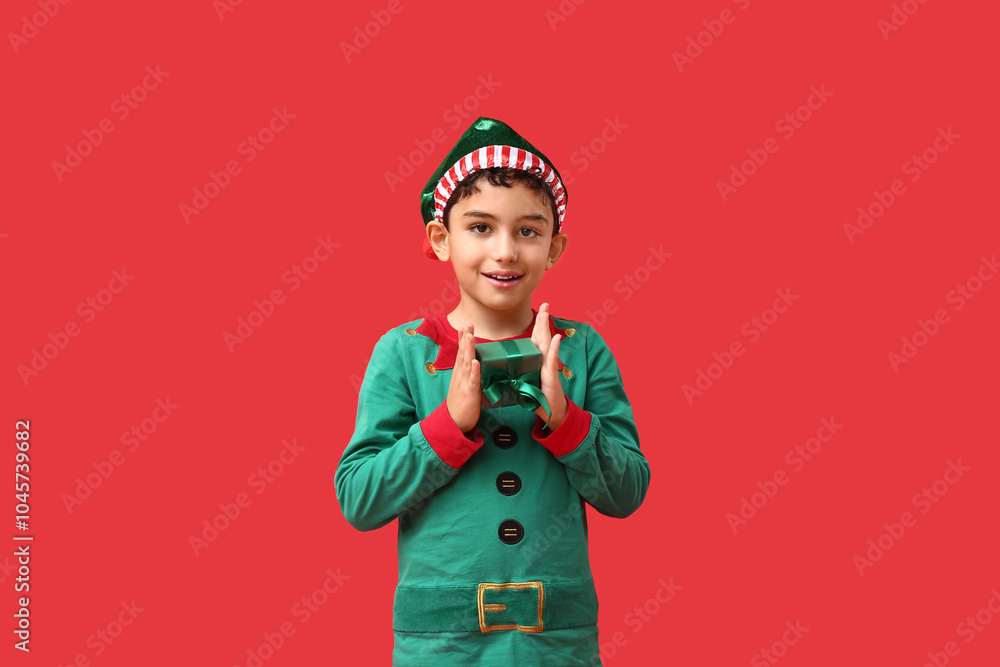 Fototapeta premium Cute little elf with Christmas gift on red background