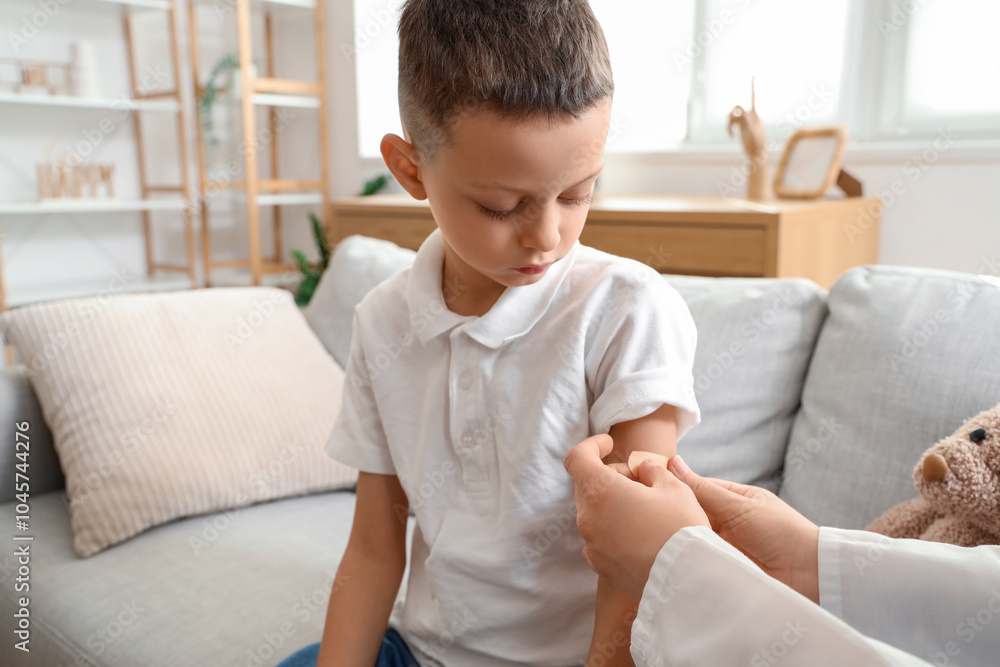 Doctor putting plaster on little boy's arm after vaccination at home Doctor putting plaster on little boy's arm after vaccination at home