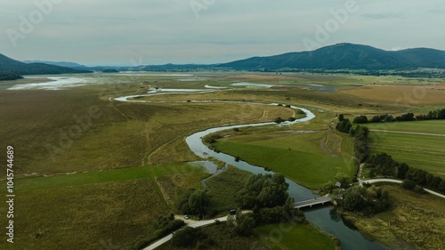 Winding river snakes through a vast, green landscape dotted and Cerknica intermittent lake, Slovenia