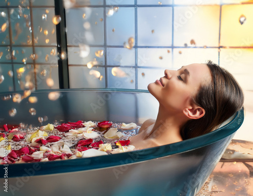 Frau in einer Badewanne mit Blüptenblätter auf dem Wasser