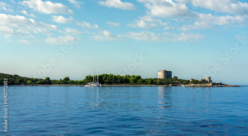 Yacht in the sea against the backdrop of rocks with dense vegetation and an abandoned fort