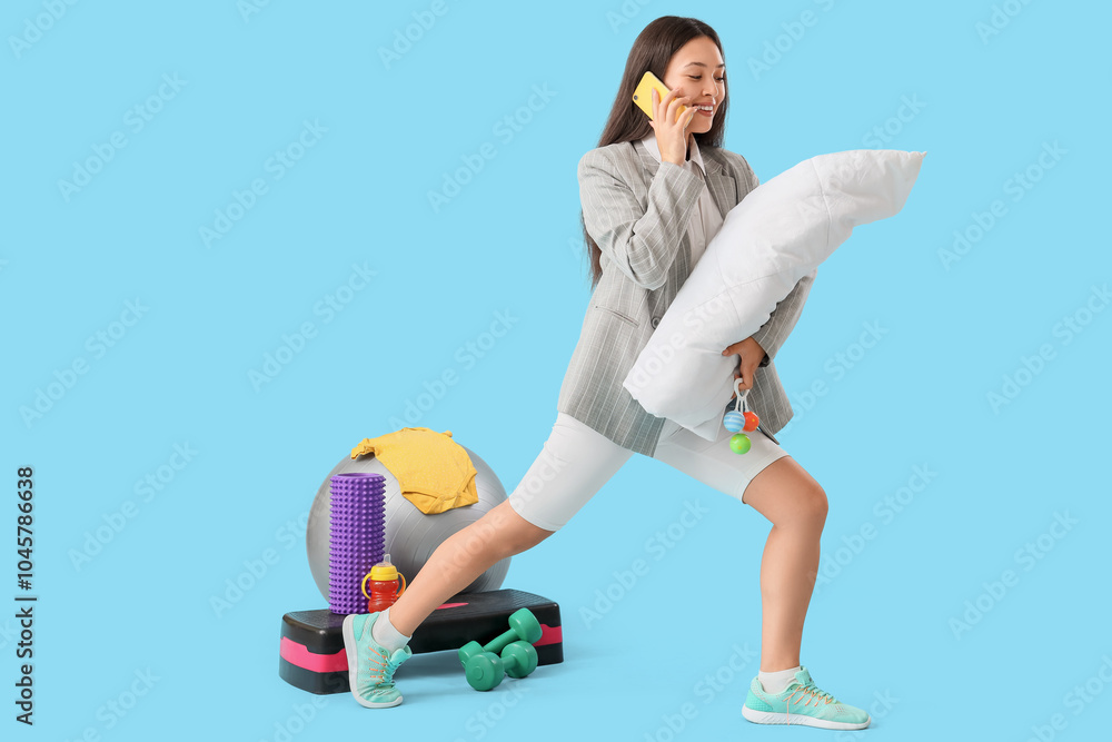 Overwhelmed Asian mother in suit with baby and toys exercising while talking by phone on blue background. Multitasking concept Overwhelmed Asian mother in suit with baby and toys exercising while talking by phone on blue background. Multitasking concept