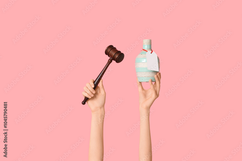 Woman holding auction gavel and antique vase on pink background Woman holding auction gavel and antique vase on pink background
