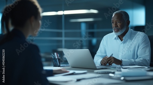 Business Meeting in Modern Office: Male Executive Consults with Female Colleague Over Laptop in a Dimly Lit Conference Room