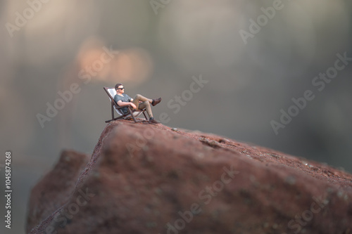 Miniature man relaxing on top of a mountain