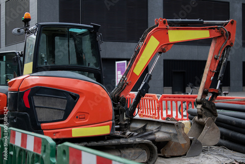 Mini excavator surrounded by blurred safety red and green pedestrian barrier in the central London. Construction machinery