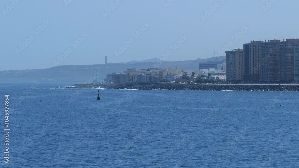 Coastal view of Gran Canaria with urban buildings along the shoreline and mountains in the background, seen from the ocean. Coastal view of Gran Canaria with urban buildings along the shoreline and mountains in the background, seen from the ocean.