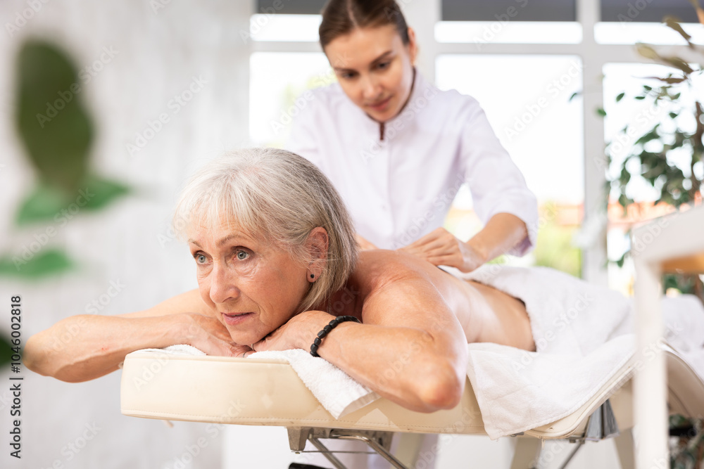Obraz premium Portrait of elderly woman enjoying relaxing massage from professional female masseur in spa center..