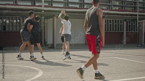 Teenage boys playing basketball on a sunny day in the schoolyard. Friends enjoying their free time together. Active lifestyle, sport, and friendship.
