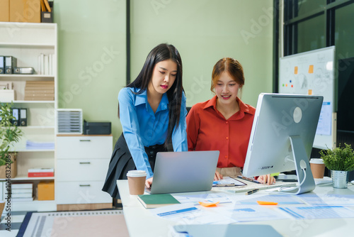 Two young female business consultants work on startup, collaborating on mobile app development social media strategies. whiteboards, documents, they aim to build a successful e-commerce business.