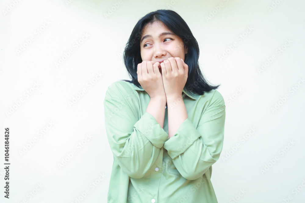 unhappy scared asian woman wearing green oversize shirt bite her nails feeling afraid and frightened looking aside to empty space thinking something standing isolated on white background