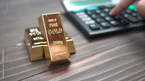 Hand view of a man using a calculator to buy gold bar. Buying gold bar for investment. Gold investment concept. Focus on gold bar, soft focus