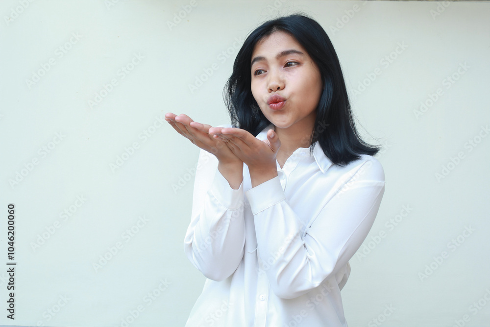 image of pretty calm asian business woman blowing kiss sending love with open palm raising near lips wearing white formal shirt standing over isolated background, candid positive expression, look away image of pretty calm asian business woman blowing kiss sending love with open palm raising near lips wearing white formal shirt standing over isolated background, candid positive expression, look away