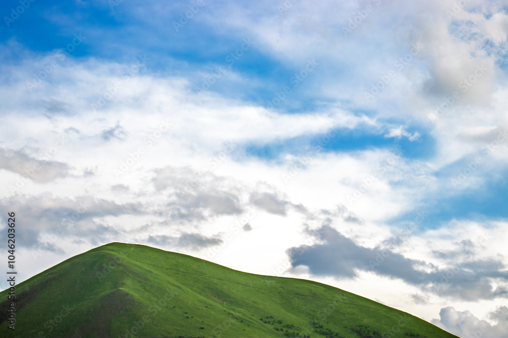 Fototapeta premium Green hill under a bright blue sky with white clouds, perfect for copy space.