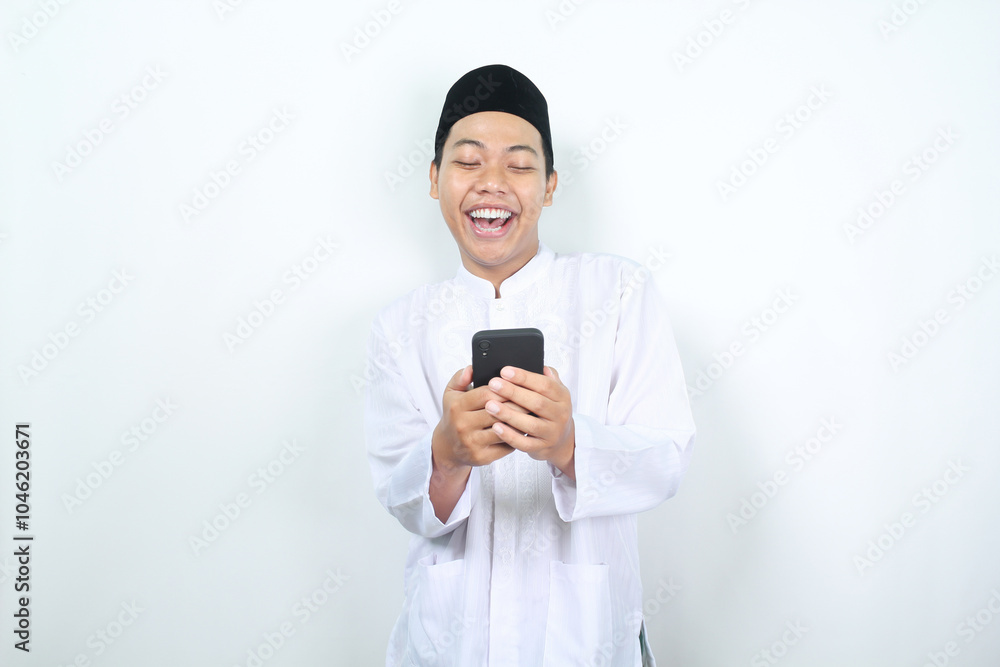 cheerful asian muslim man laughing while holding phone isolated cheerful asian muslim man laughing while holding phone isolated