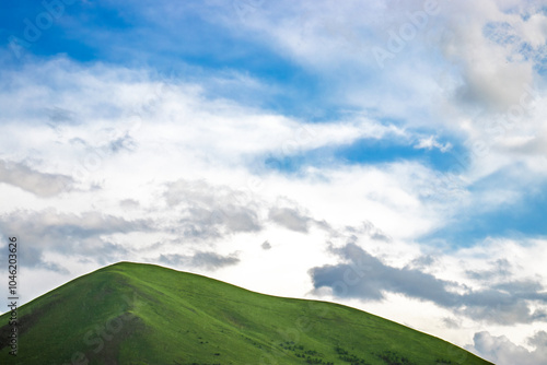 Green hill under a bright blue sky with white clouds, perfect for copy space.