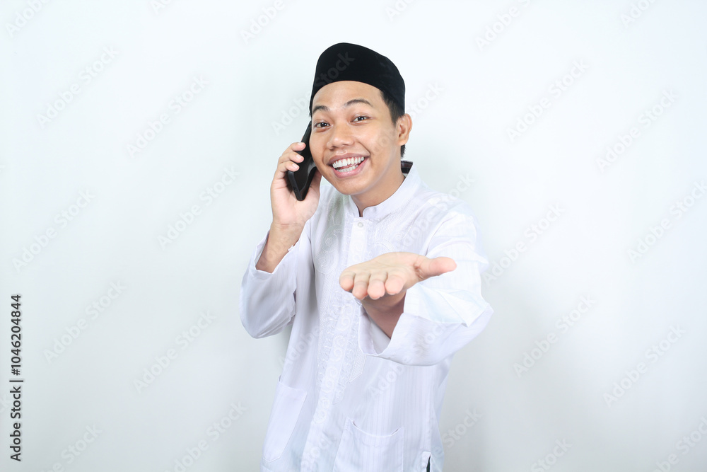 delighted asian muslim man presenting hand forward to camera with smiling face while speaking on his phone isolated delighted asian muslim man presenting hand forward to camera with smiling face while speaking on his phone isolated
