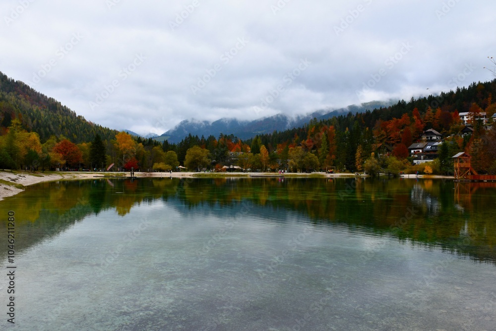 Fototapeta premium Shore of lake Jasna near Kranjska Gora in Gorenjska, Slovenia with a reflection in the water and yellow and red trees,
