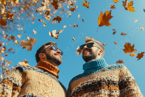 Gay couple or two boyfriends smiling in golden autumn leaves. Romantic walk, happy couple with warm pullovers in autumn park. Sunny weather hipster people Smiling friends hugging in falling leaves. photo