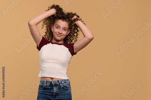 A young girl playfully holding her hair up, smiling cheerfully against a beige background. photo