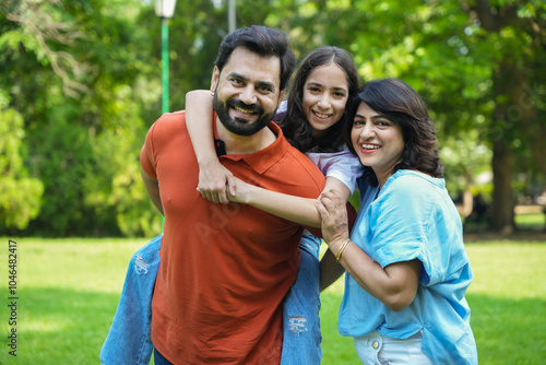 young Indian father carrying, piggyback his daughter in the park. family of three enjoying vacation in garden. bonding together and playful interaction. photo