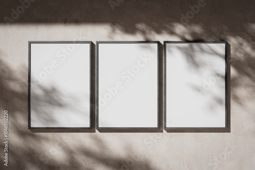 Three blank white portrait A0 posters in a metal frame on a plaster wall