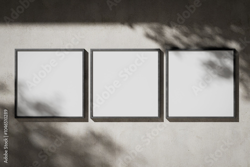 Three white blank square posters in a metal frame on a plaster wall