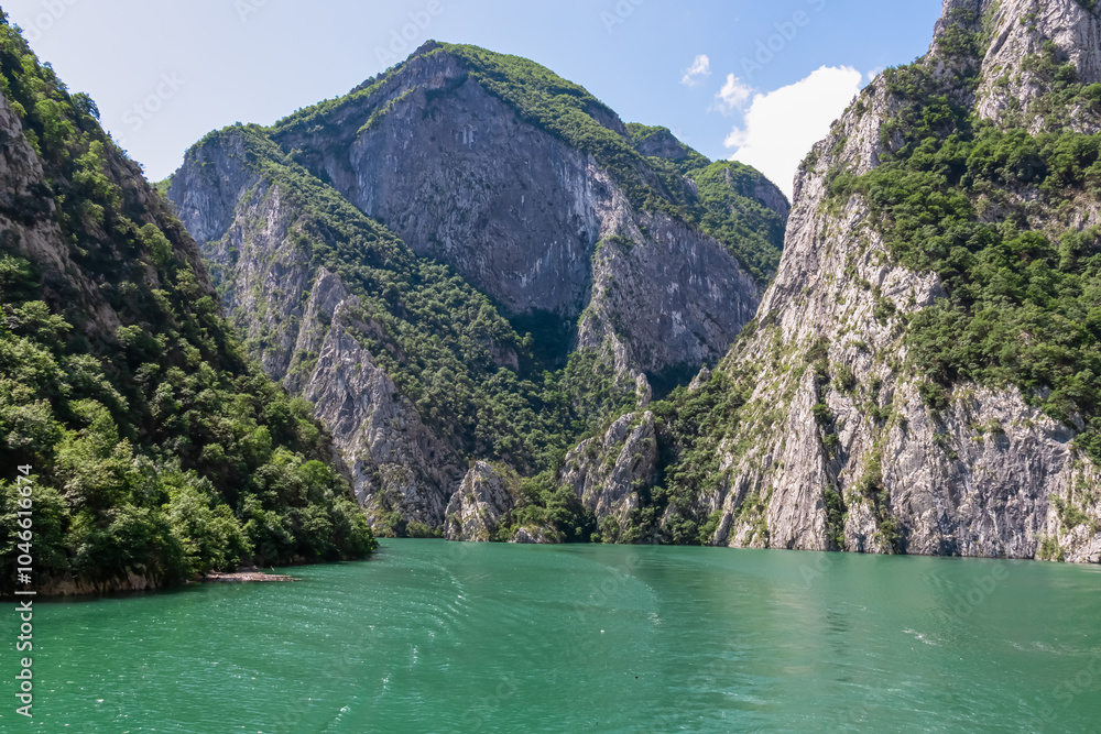 Scenic ferry boat tour on Lake Koman reservoir on Drin river surrounded by forested steep hills, cliffs and majestic rugged mountain ranges of Albanian Alps. Panoramic view along Albanian Fjords. Awe Scenic ferry boat tour on Lake Koman reservoir on Drin river surrounded by forested steep hills, cliffs and majestic rugged mountain ranges of Albanian Alps. Panoramic view along Albanian Fjords. Awe