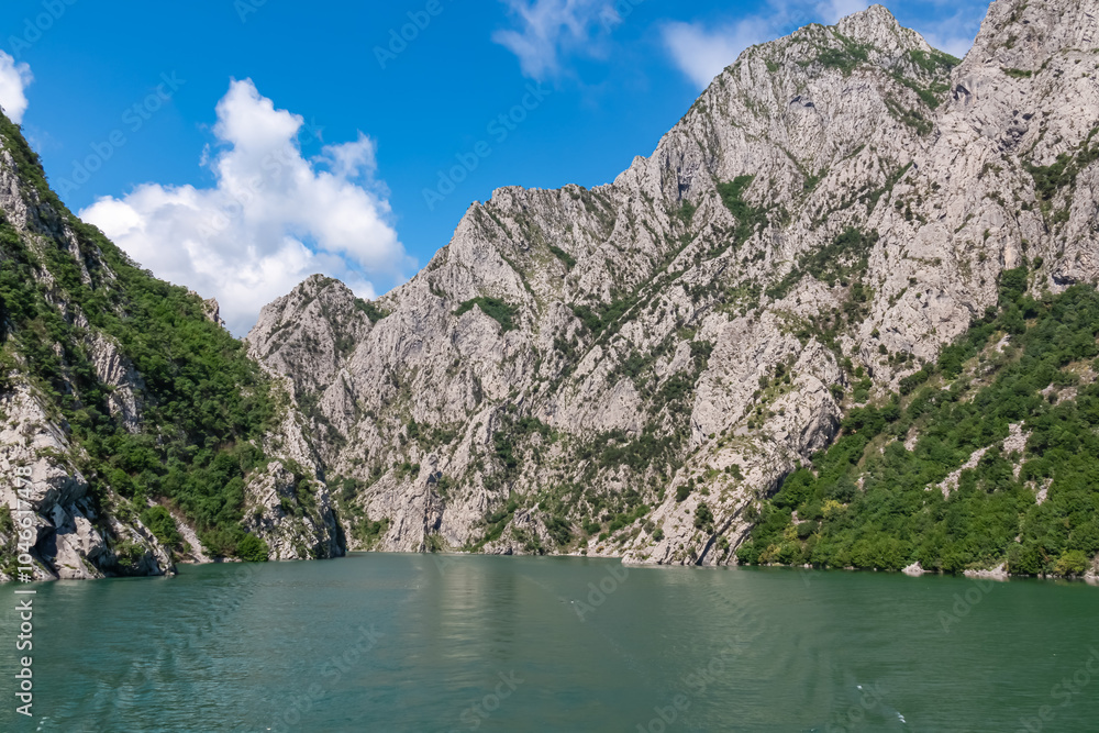 Scenic ferry boat tour on Lake Koman reservoir on Drin river surrounded by forested steep hills, cliffs and majestic rugged mountain ranges of Albanian Alps. Panoramic view along Albanian Fjords. Awe Scenic ferry boat tour on Lake Koman reservoir on Drin river surrounded by forested steep hills, cliffs and majestic rugged mountain ranges of Albanian Alps. Panoramic view along Albanian Fjords. Awe