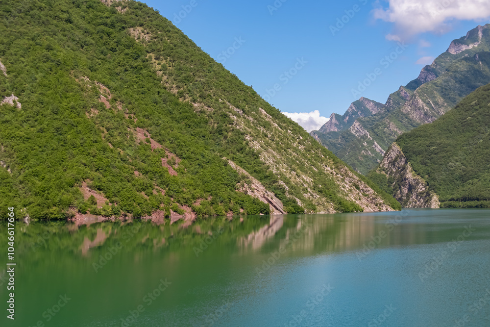 Scenic ferry boat tour on Lake Koman reservoir on Drin river surrounded by forested steep hills, cliffs and majestic rugged mountain ranges of Albanian Alps. Panoramic view along Albanian Fjords. Awe Scenic ferry boat tour on Lake Koman reservoir on Drin river surrounded by forested steep hills, cliffs and majestic rugged mountain ranges of Albanian Alps. Panoramic view along Albanian Fjords. Awe