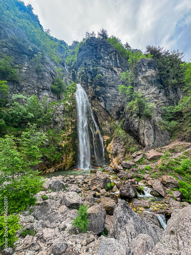 Majestic Grunas waterfall cascading down a rocky cliff in Albanian Alps, Thethi National Park, Northern Albania. Idyllic plunge pool below surrounded by lush green vegetation. Mist created by water photo