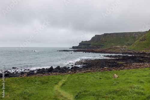 Tourists explore the rocky cliffs and shoreline of Giant's Causeway, Northern Ireland, as the Atlantic Ocean stretches under grey clouds