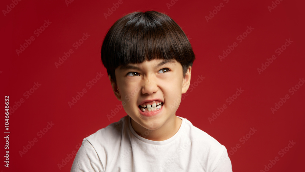 Child displays fierce, energetic expression, teeth showing in moment of pure intensity against bold red studio background. Concept of facial-expressions, positive and negative emotions. Ad Child displays fierce, energetic expression, teeth showing in moment of pure intensity against bold red studio background. Concept of facial-expressions, positive and negative emotions. Ad