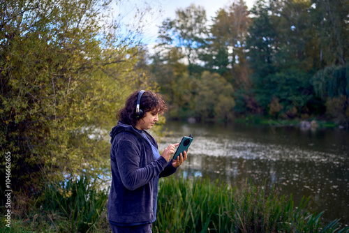 middle-aged woman exercising and switching music in her wireless headphones using her phone during a morning jog in an autumn park photo