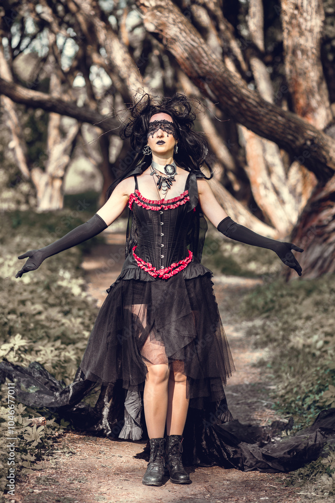 Naklejka premium A young woman in the image of a witch and sorceress, standing in a dark forest, wearing a black dress with a train and a socket on her head.