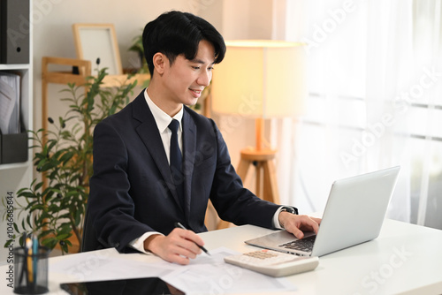 Handsome businessman in black suit analyzing data on laptop in modern workplace