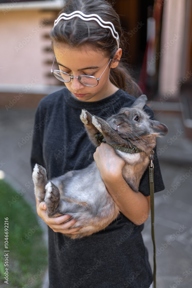 A girl plays with a domestic rabbit on the street. Pet concept. A girl plays with a domestic rabbit on the street. Pet concept.