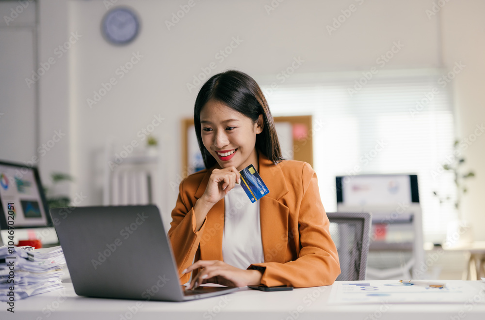Asian businesswoman is smiling while using her laptop for online shopping at the office. She is holding a credit card in her hand, ready to enter her payment information Asian businesswoman is smiling while using her laptop for online shopping at the office. She is holding a credit card in her hand, ready to enter her payment information
