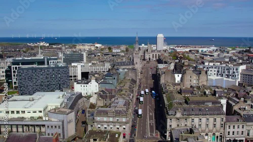 A drone captures Aberdeen’s city streets stretching toward the North Sea, with a clear view of offshore wind turbines and historic architecture. The vibrant coastal cityscape is highlighted from above