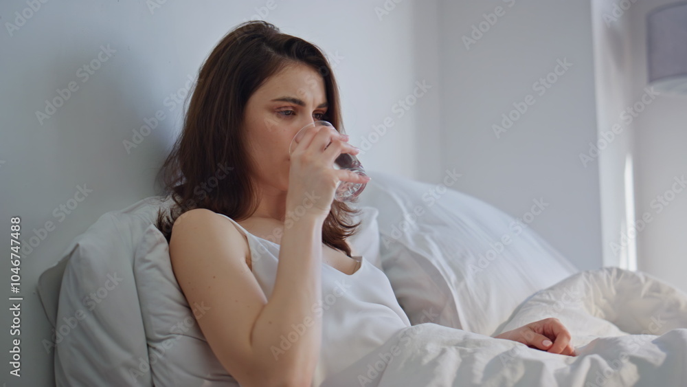 Unhealthy brunette drinking water from glass sitting bed early morning closeup. Unhealthy brunette drinking water from glass sitting bed early morning closeup.