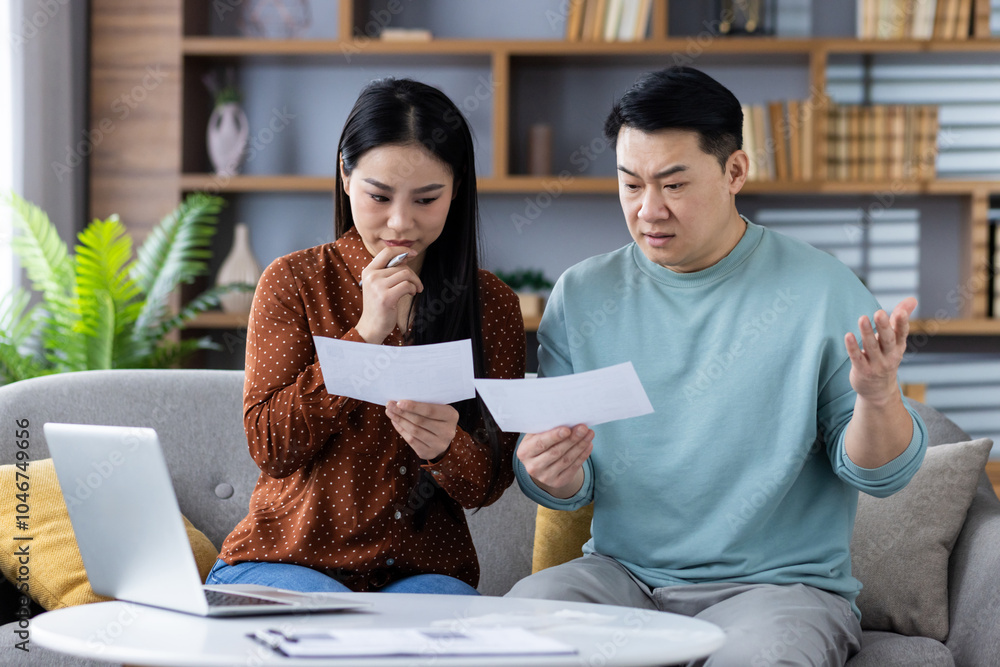 © Liubomir - Asian couple checking financial documents, looking concerned while discussing expenses at home. Man and woman focus on paperwork and stress about finances with laptop nearby. © Liubomir - Asian couple checking financial documents, looking concerned while discussing expenses at home. Man and woman focus on paperwork and stress about finances with laptop nearby.