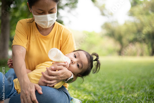 Asian daughter drinking milk in a bottle Sleep happily on mom's lap in the park on the weekend